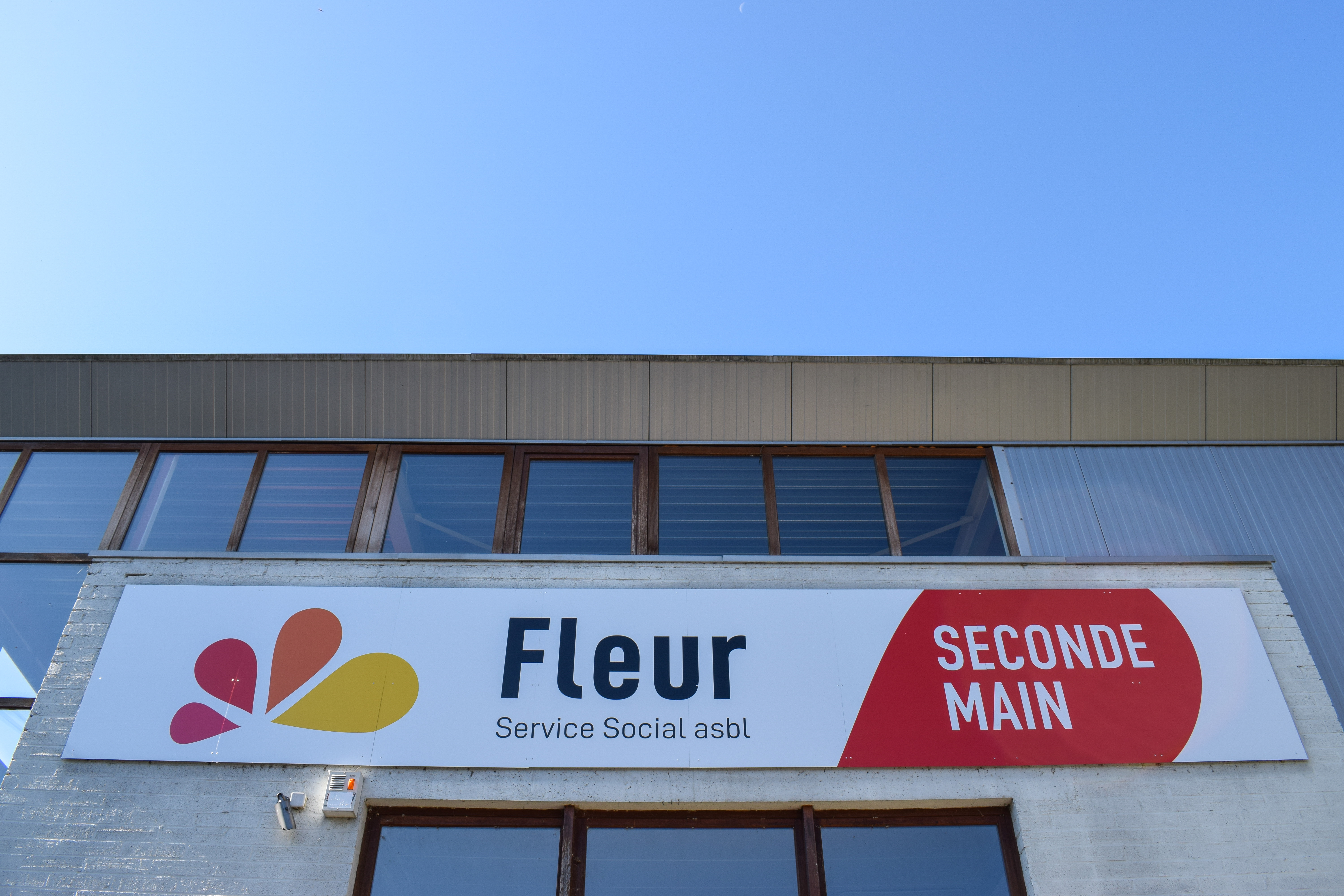 Façade de magasin de seconde main Fleur Service Social asbl devant un ciel bleu