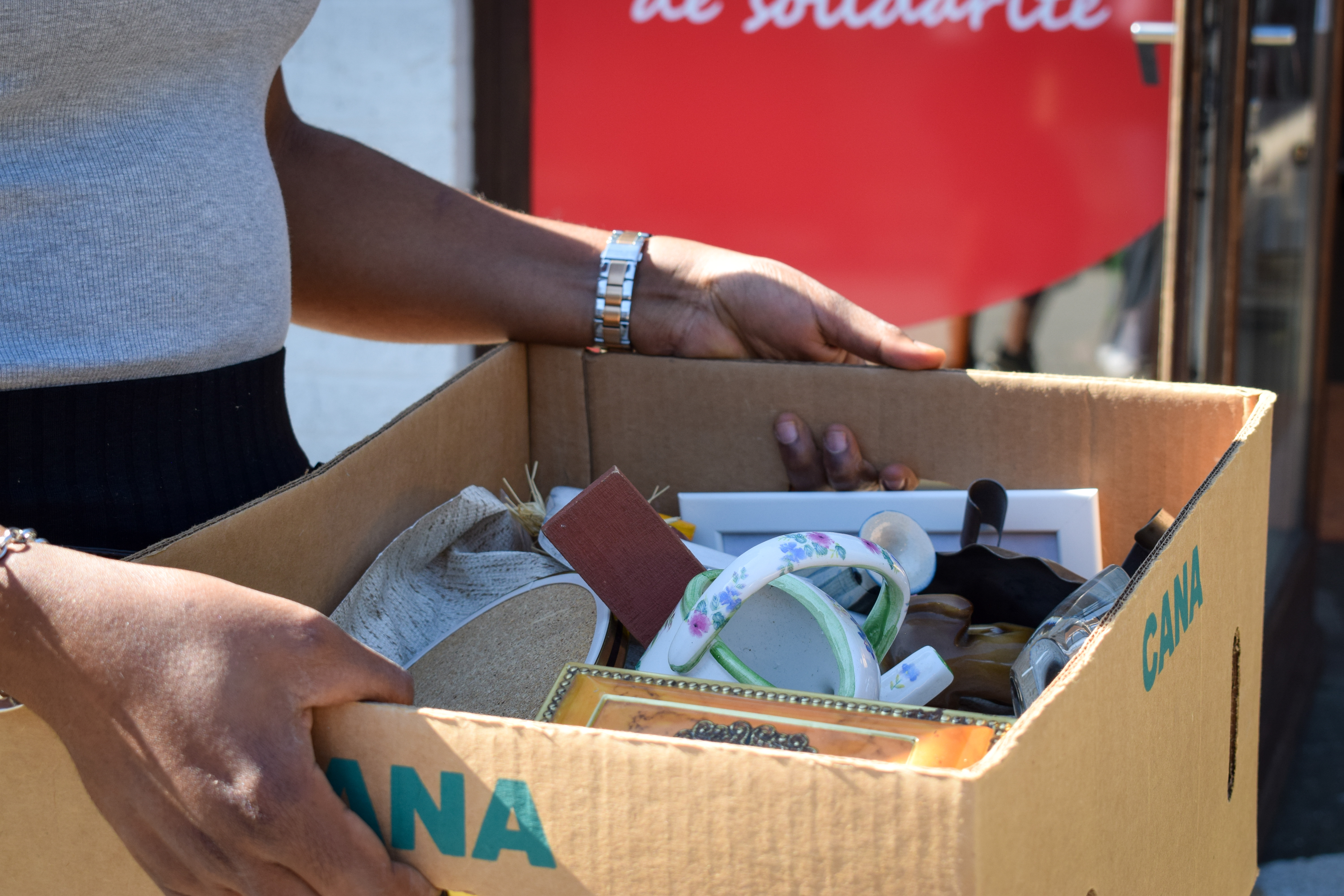 Une dame tient dans ses mains une caisse en carton remplie de bibelots pour la collecte de dons